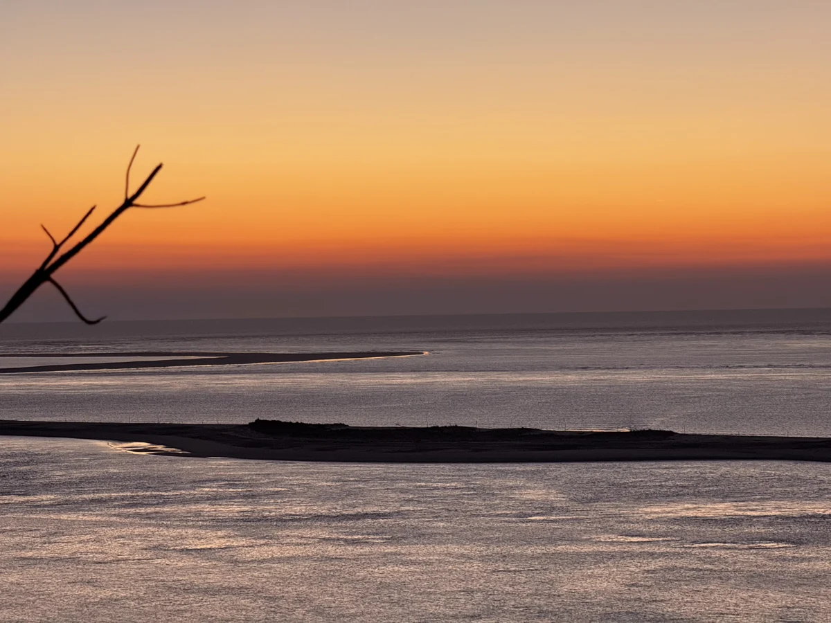 An ochre and red sky above the water and sandbanks
